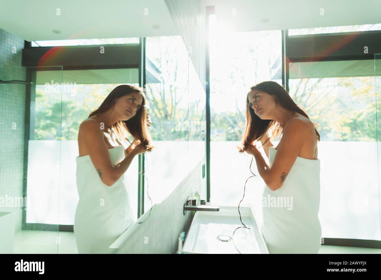 Femme enveloppée dans une serviette sèche-cheveux dans un miroir ensoleillé de salle de bains Banque D'Images