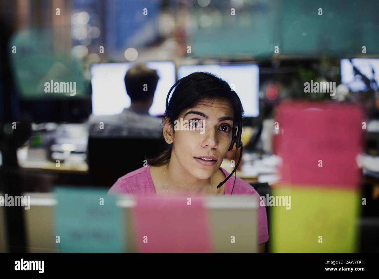 Femme d'affaires avec micro-casque regardant les notes adhésives, la planification au bureau Banque D'Images