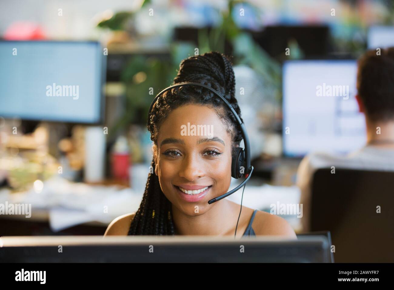 Portrait d'une femme d'affaires confiante avec micro-casque/oreillette sur un ordinateur au bureau Banque D'Images