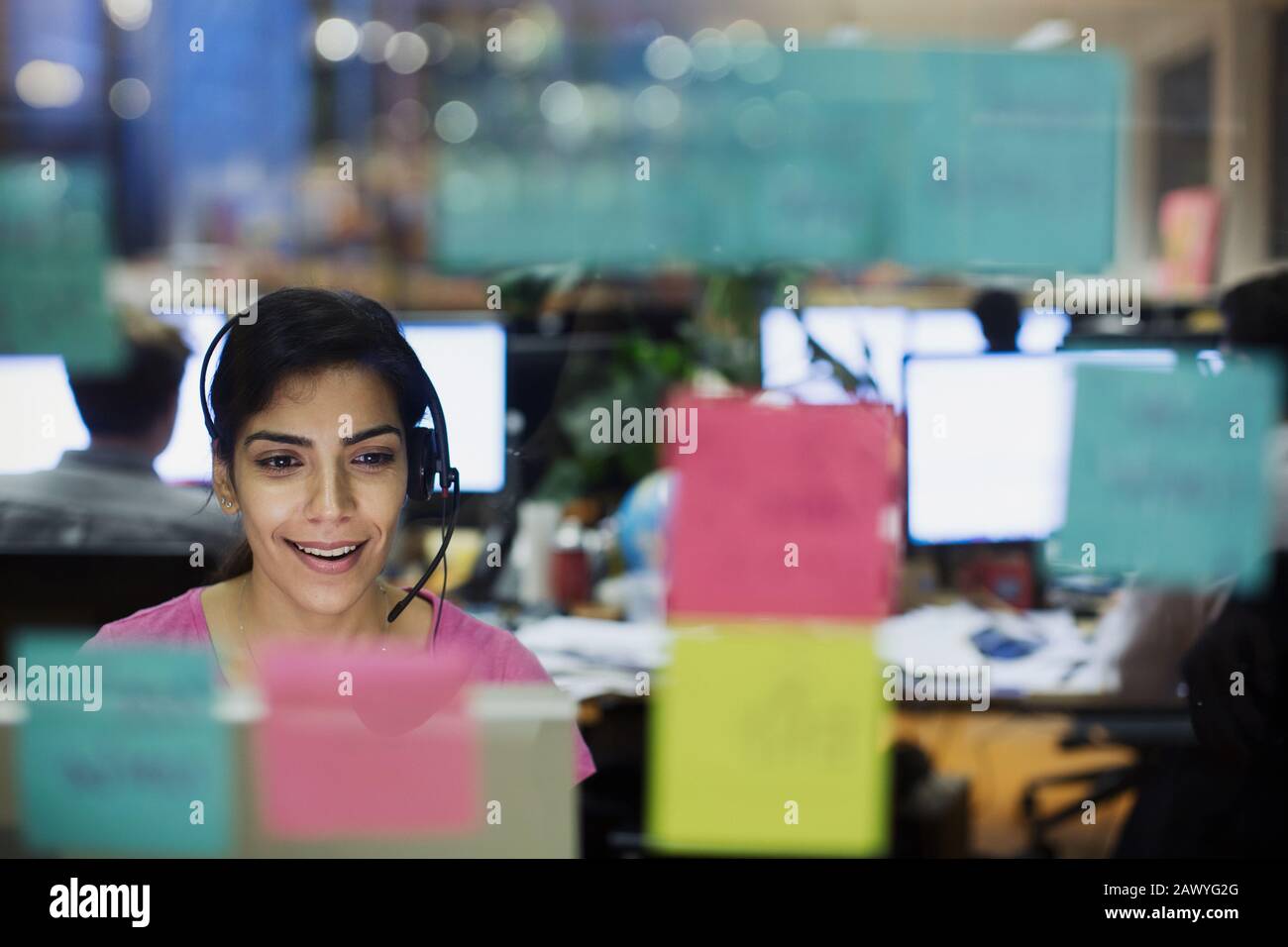 Femme d'affaires avec micro-casque travaillant sur un ordinateur au bureau derrière des notes adhésives Banque D'Images