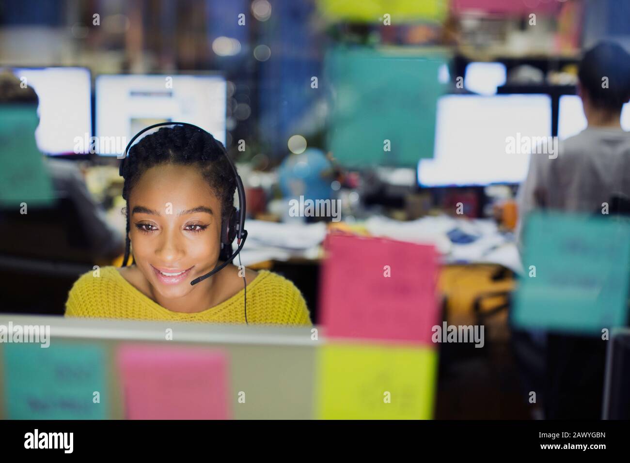 Femme d'affaires avec micro-casque travaillant sur ordinateur derrière des notes adhésives Banque D'Images