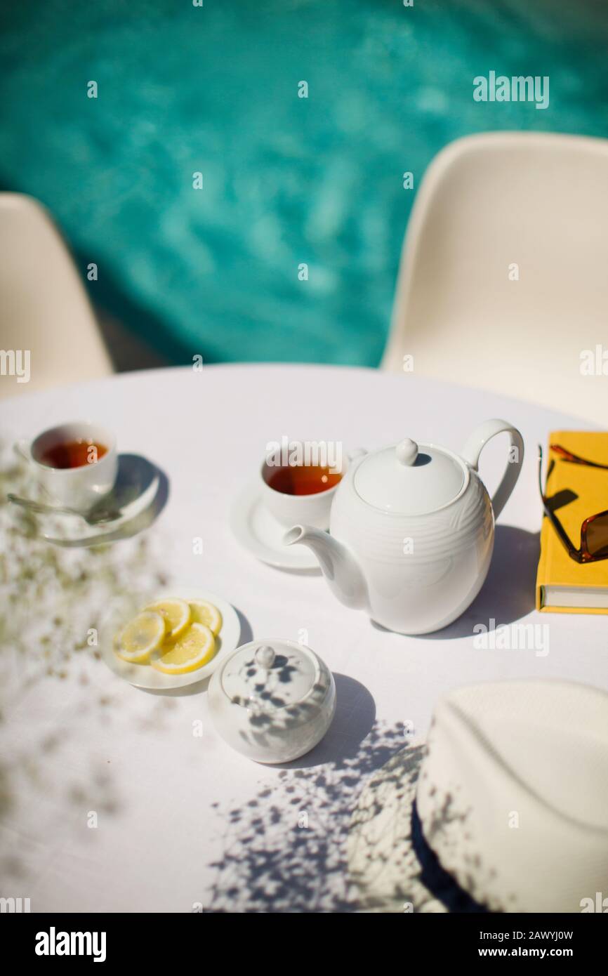 Service de thé sur la table ensoleillée de terrasse en bordure de piscine en été Banque D'Images