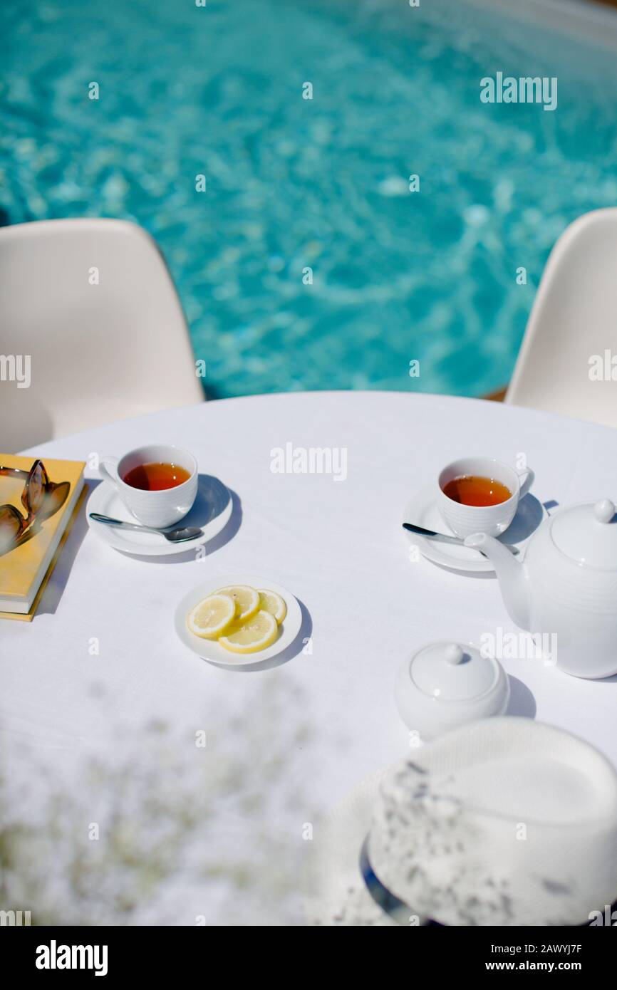 Service de thé sur la table ensoleillée de terrasse en bordure de piscine en été Banque D'Images