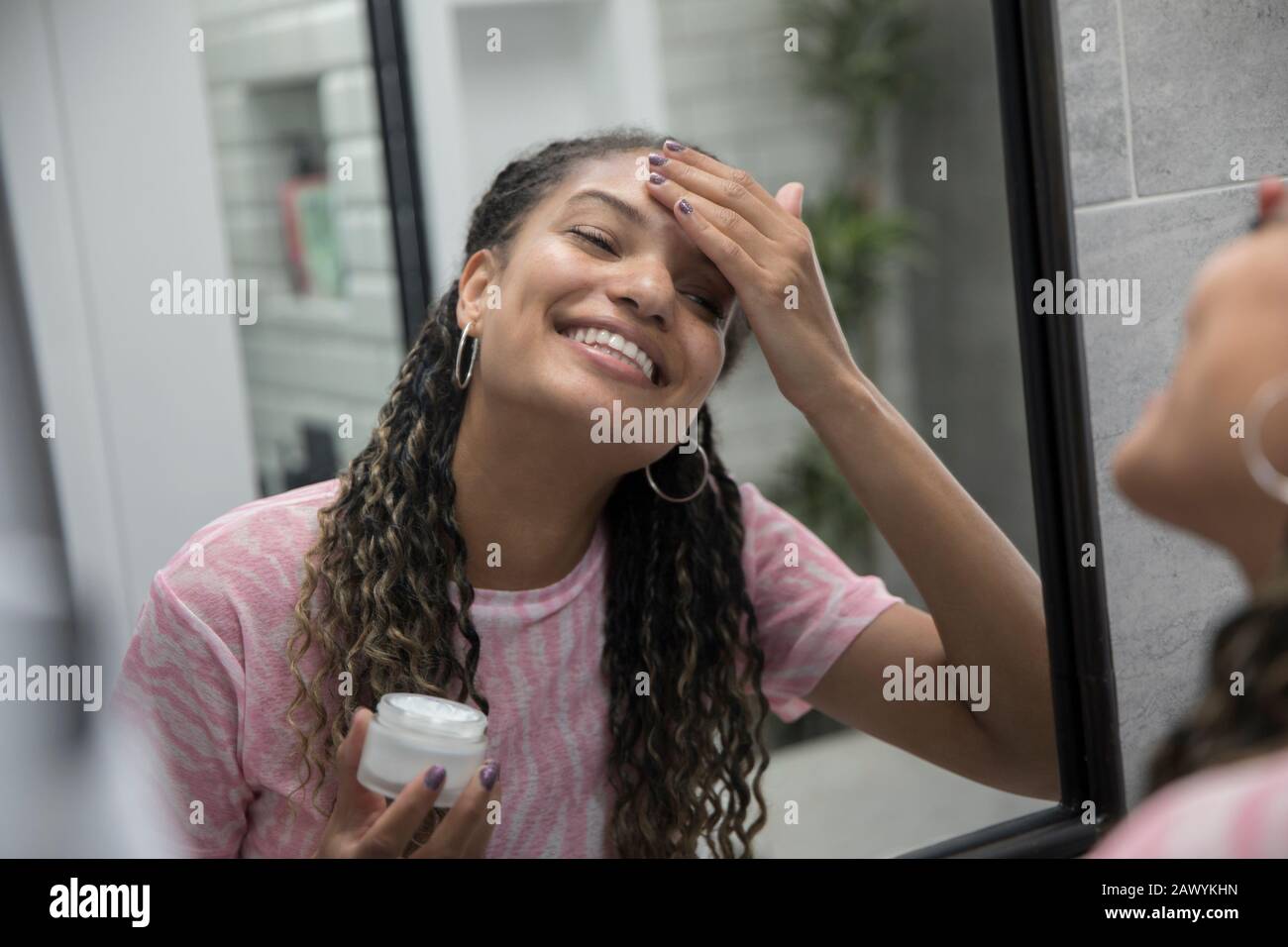 Heureuse jeune femme appliquant l'hydratant dans le miroir de salle de bains Banque D'Images