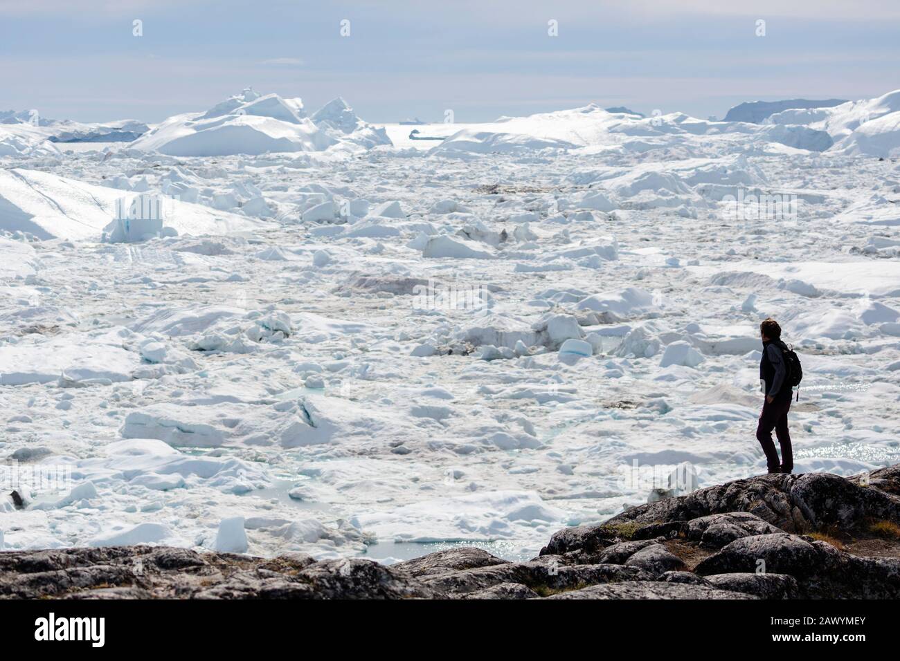Homme sur les rochers regardant la glace de glacier ensoleillée vue fondre Groenland Banque D'Images