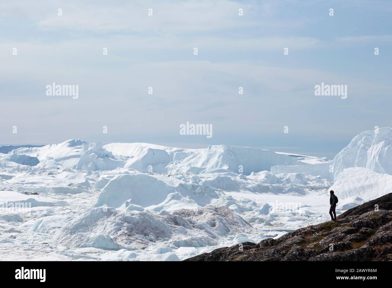 Homme debout sur la falaise surplombant la fonte des glaces glaciaires Groenland Banque D'Images