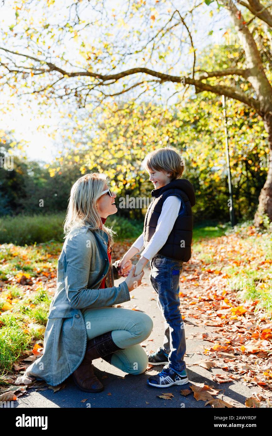 Mère et fils tenant les mains et parlant dans le parc ensoleillé d'automne Banque D'Images