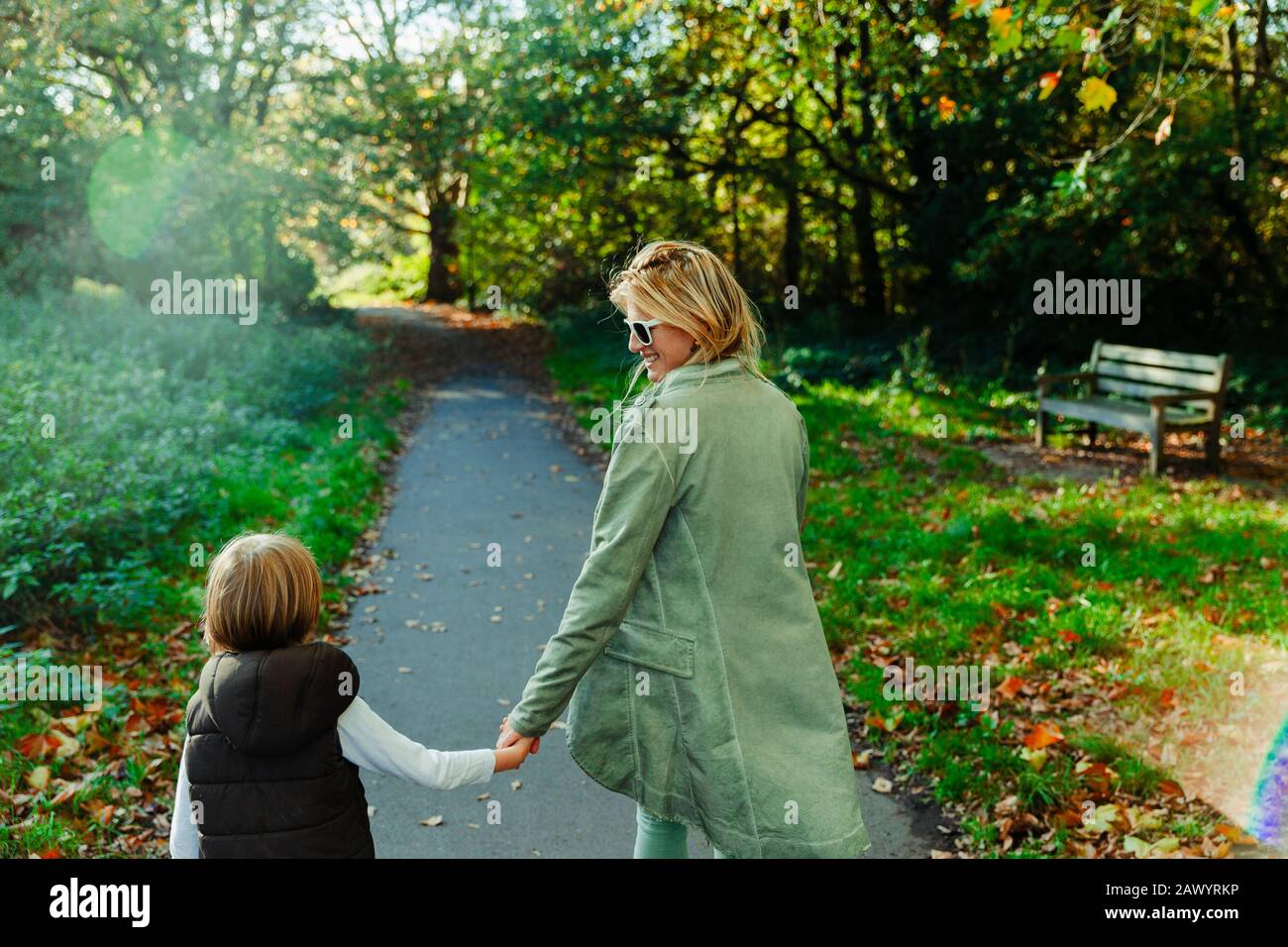 Bonne mère et fils tenant les mains et marchant dans le parc ensoleillé d'automne Banque D'Images
