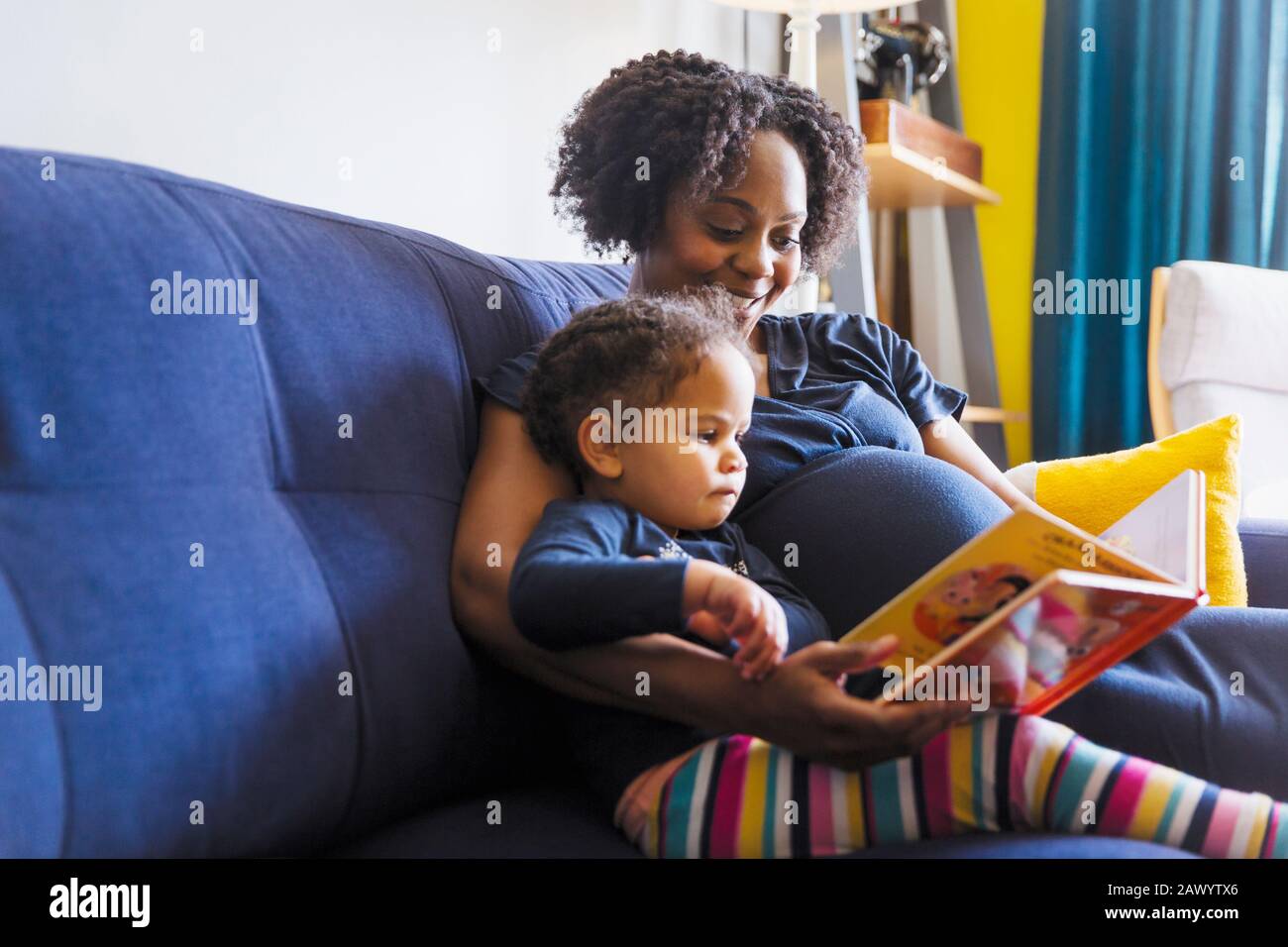 La mère enceinte et la fille lisent le livre sur le canapé Banque D'Images