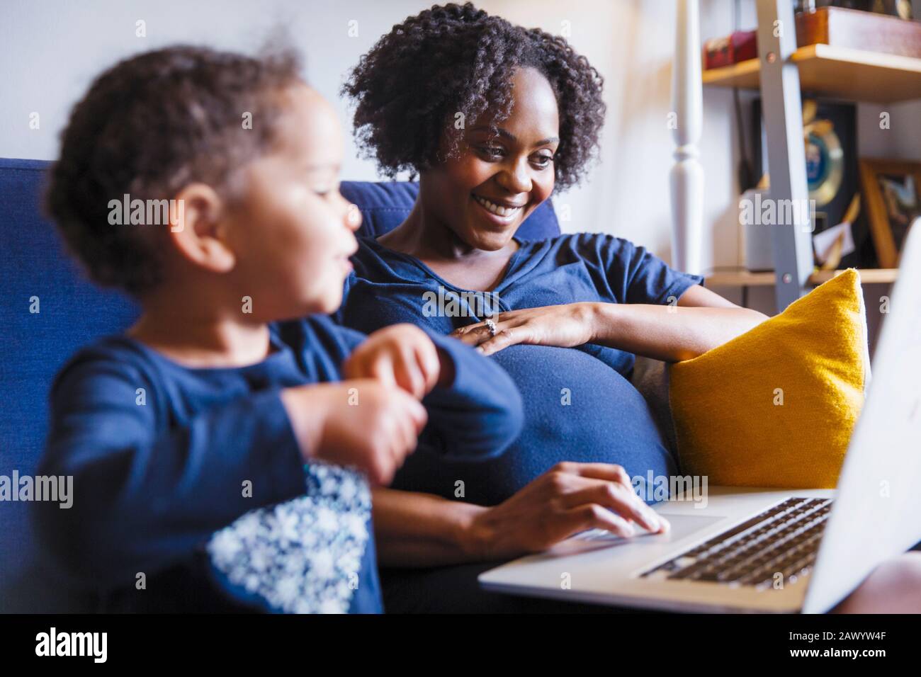 Bonne femme enceinte avec fille utilisant un ordinateur portable sur un canapé Banque D'Images