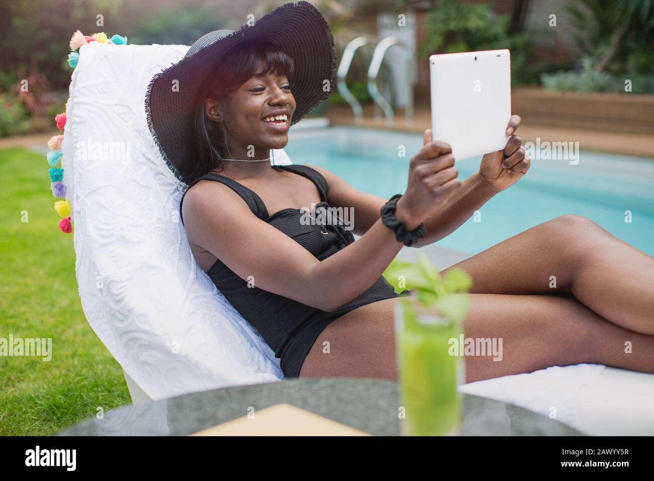 Bonne jeune femme discutant vidéo avec une tablette numérique au bord de la piscine Banque D'Images