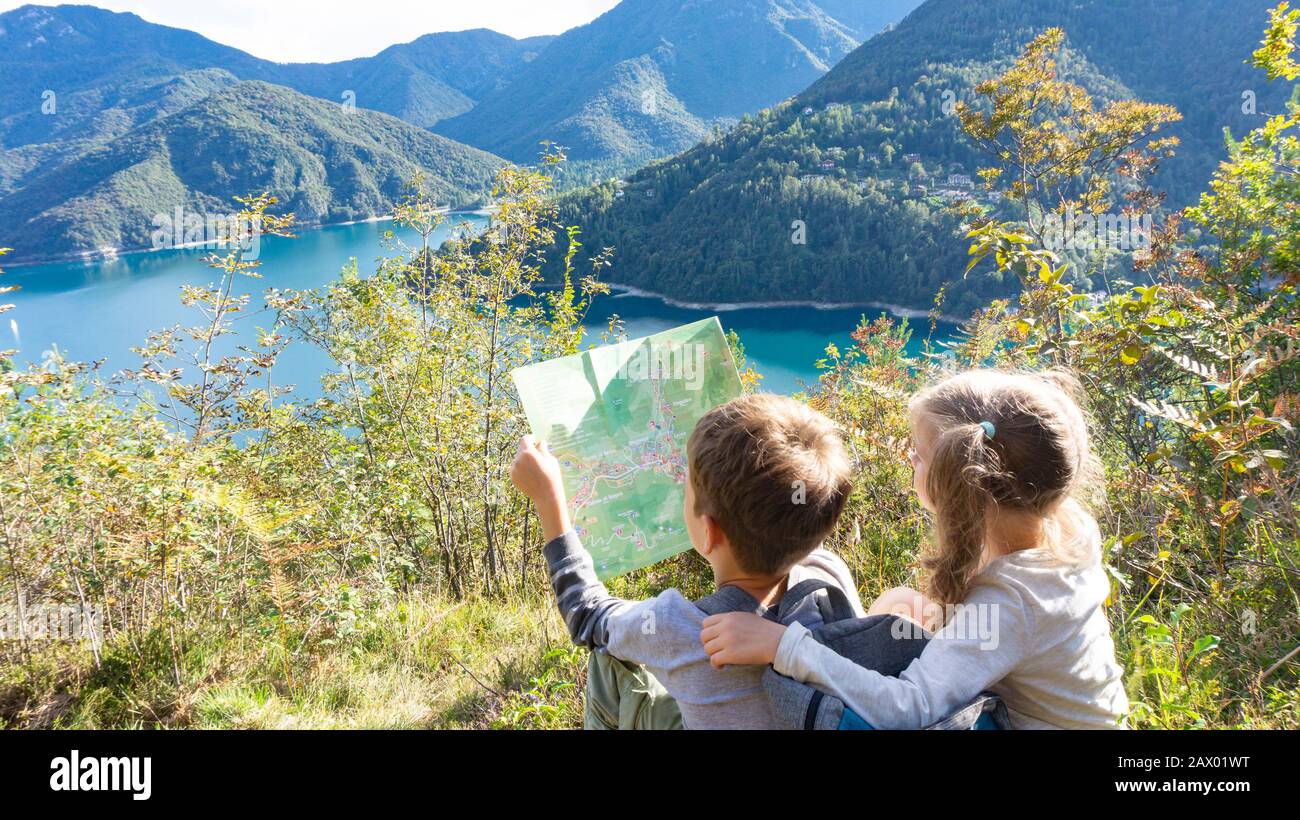 Deux jeunes enfants avec une carte planifient leur itinéraire de randonnée vers un camping dans la forêt sur la rive d'un lac de montagne bleu. Banque D'Images