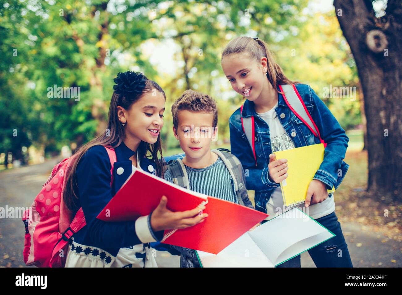 Retour à l'école. Les enfants avec des sacs à dos ont du plaisir, de parler, de lire un livre.Groupe d'écoliers élémentaires ayant une discussion sur les devoirs pendant leur déplacement Banque D'Images