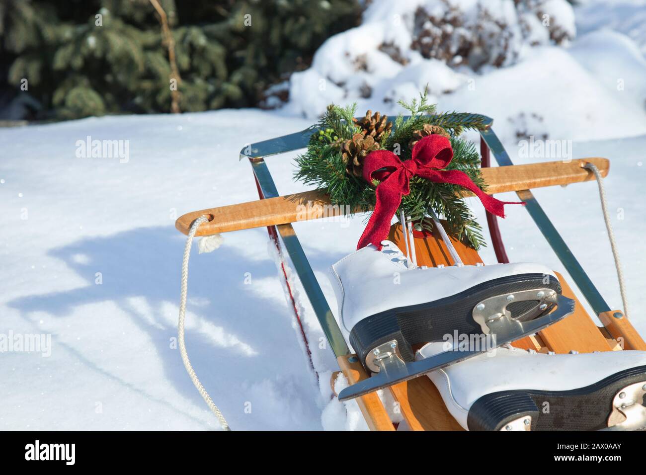 Traîneaux vintage dans la neige avec couronne et noeud rouge et patins blancs le jour ensoleillé Banque D'Images