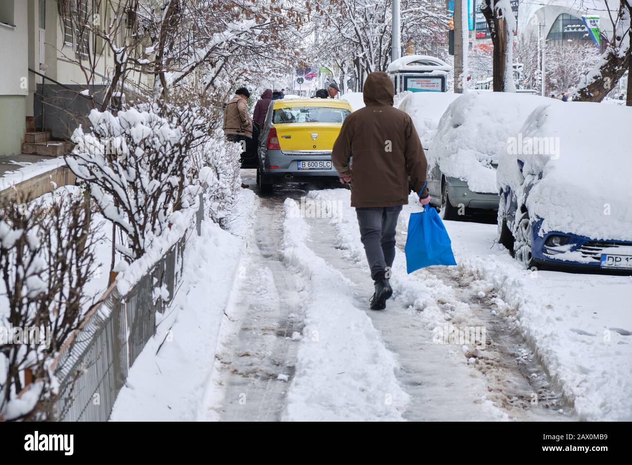 Bucarest, Roumanie - 6 février 2020: Trottoir de Bucarest en hiver avec des voitures garées illégalement, recouvertes de neige, et une voiture jaune Dacia bloquant pe Banque D'Images