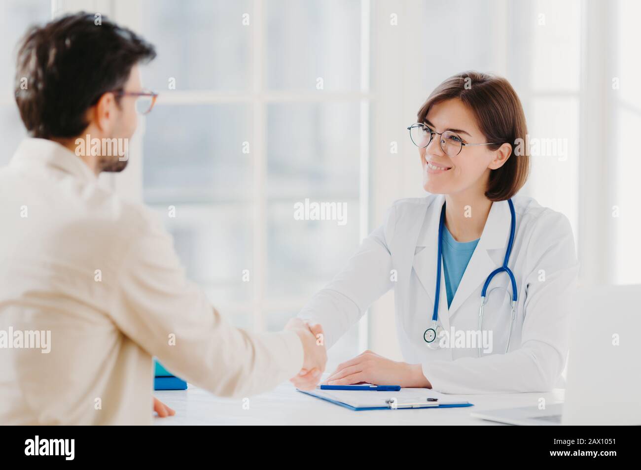 Le médecin amical salue le patient avec la poignée de main, pose dans une clinique privée, s'asseoir en face, ont parler, accepter de signer le contrat d'assurance, moi Banque D'Images