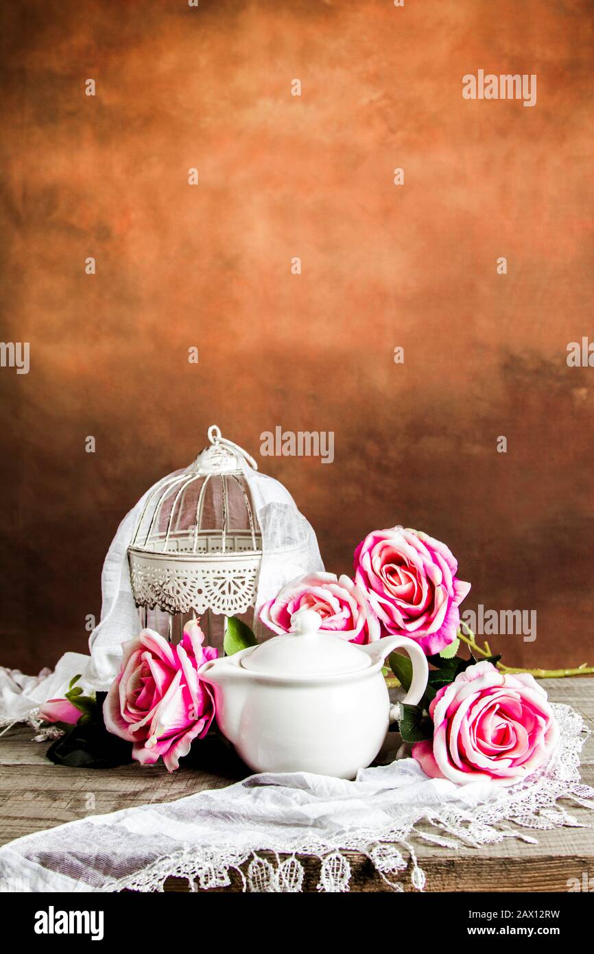 Cage blanche et théière avec roses et décoration sur une table en bois Banque D'Images