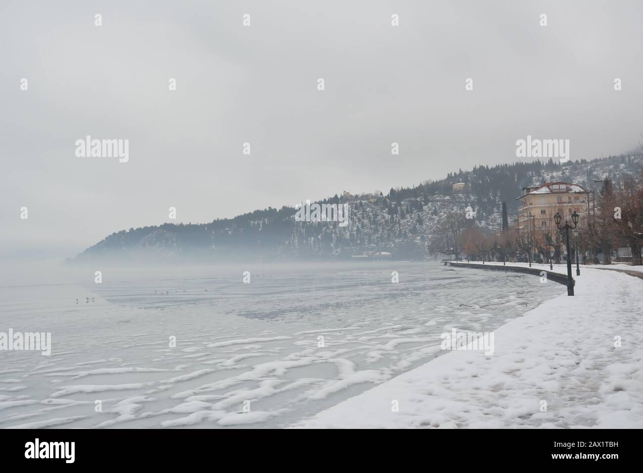 Allée piétonne recouverte de neige sur les rives du lac gelé Orestiada à Kastoria, en Grèce, une journée de brume surcousue Banque D'Images