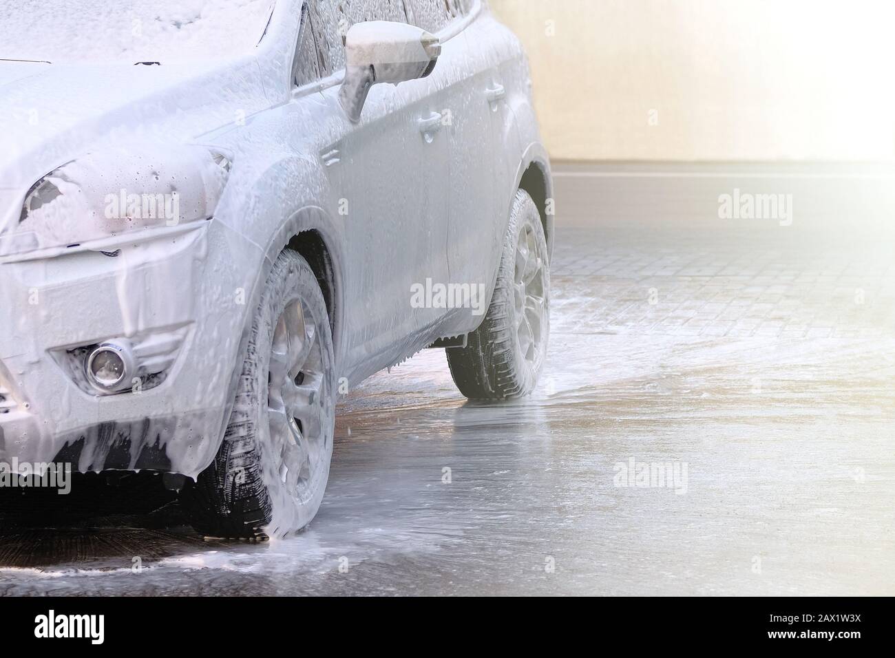 Modelage avec mousse sur la voiture dans le lavage de voiture en libre-service. Voiture blanche à la station de lavage de voiture. De l'eau et du savon blanc coule. Banque D'Images