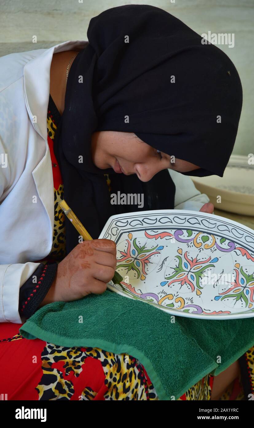 Un artisan marocain utilisant des méthodes traditionnelles pour peindre et glacer une plaque de céramique dans un atelier traditionnel de poterie, Fès, Maroc, Afrique. Banque D'Images