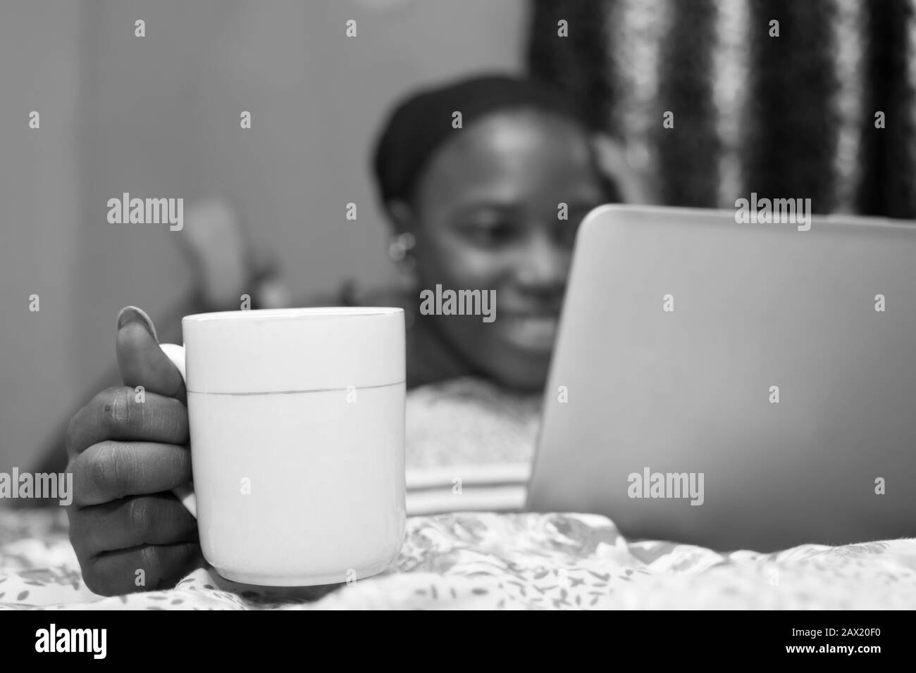 jolie dame africaine à la maison seule dans sa chambre, regarder un film sur son ordinateur portable, flou, avec tasse de café au foyer Banque D'Images
