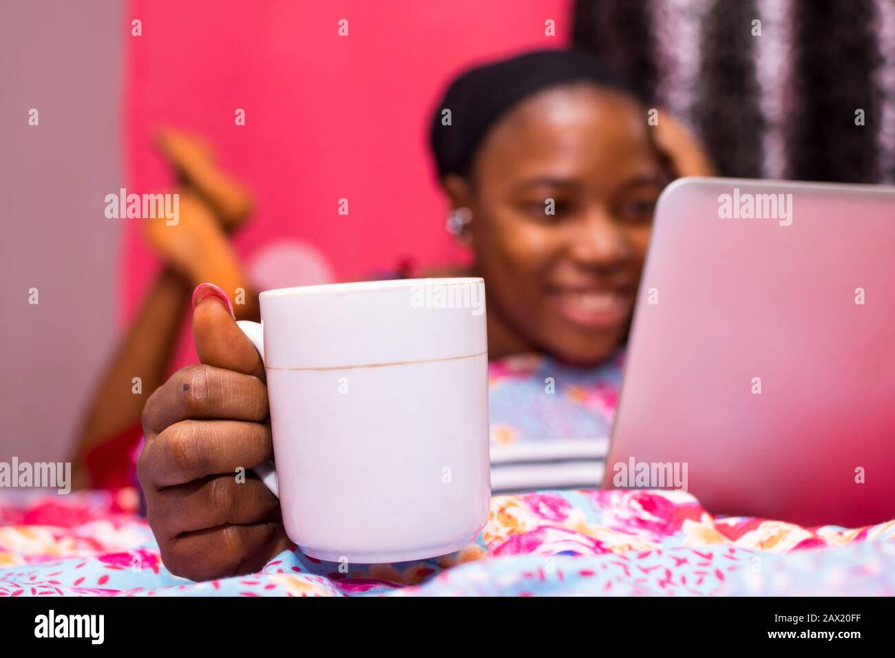 jolie dame africaine à la maison seule dans sa chambre, regarder un film sur son ordinateur portable, flou, avec tasse de café au foyer Banque D'Images