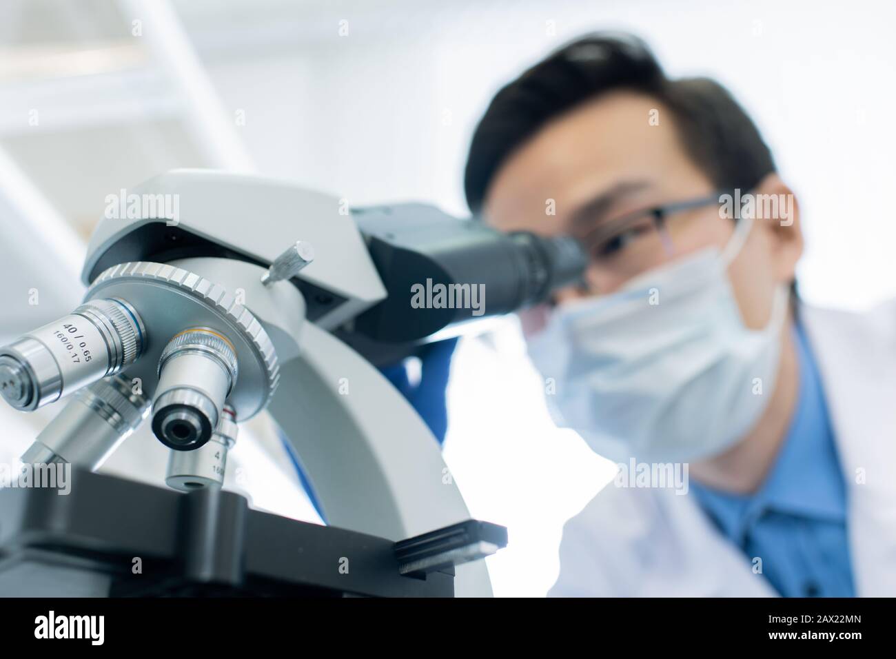 Pharmacologue mâle non reconnaissable examinant l'échantillon au microscope en laboratoire moderne, prise horizontale Banque D'Images