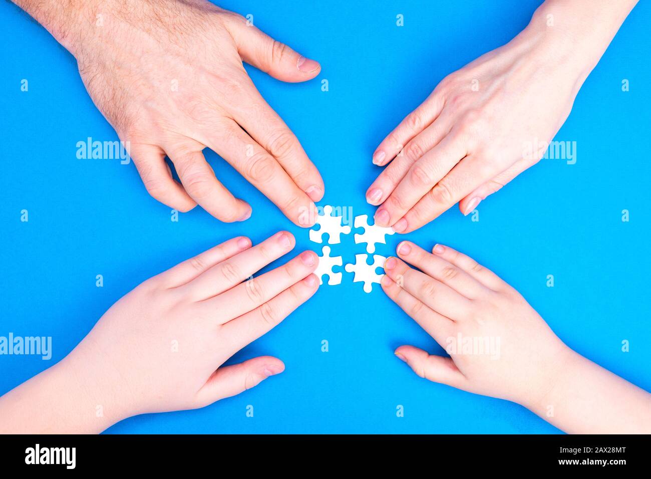 Les mains de l'homme, de la femme et des enfants collectent un puzzle sur un fond bleu. Image conceptuelle de la coopération conjointe dans la famille. Vue de dessus Banque D'Images