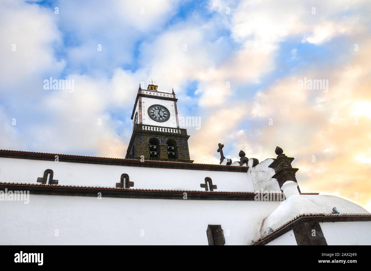 La façade extérieure de l'église Saint-Sébastien, Igreja Matriz de Sao Sebastiao, à Ponta Delgada, Açores, Portugal. Tour d'horloge blanche du dessous avec ciel bleu et nuages au-dessus. Coucher de soleil nuages. Banque D'Images