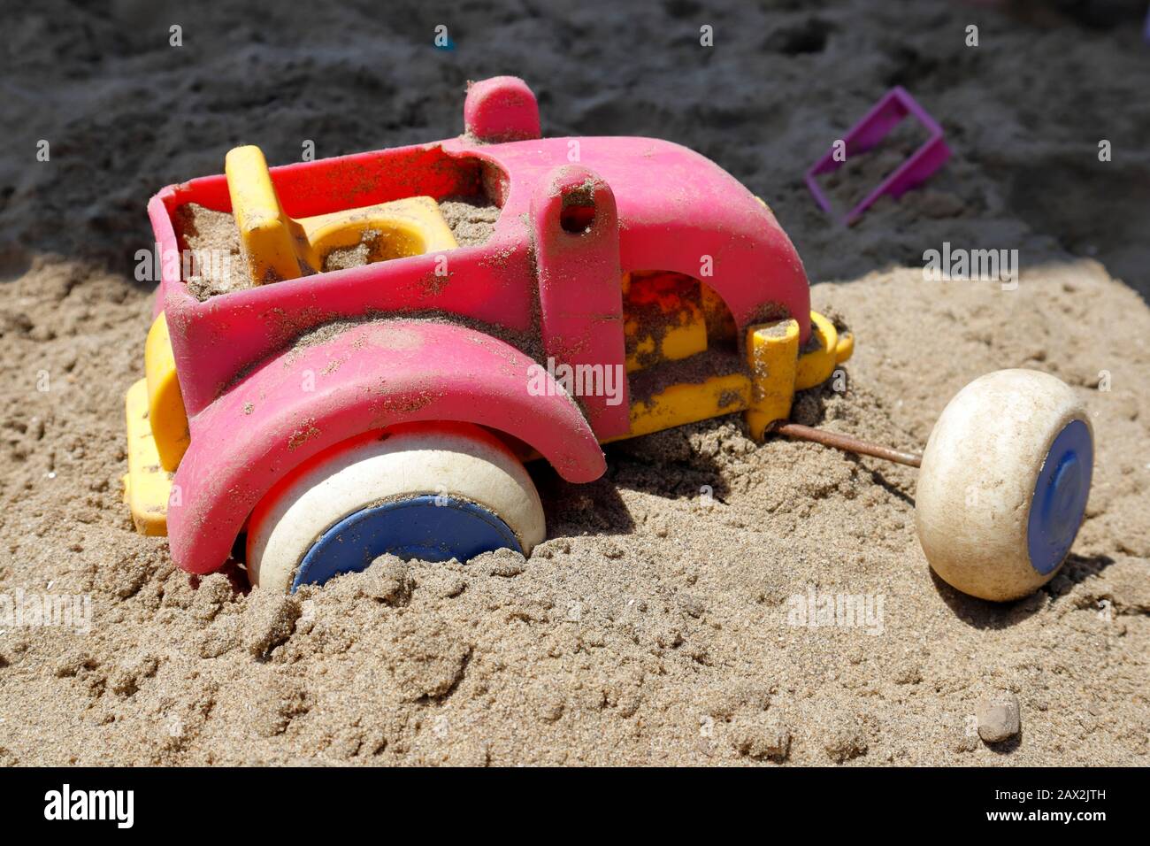 Les roues se sont détournées ! Coincé dans une rut, ce tracteur jouet dans la fosse à sable semble avoir trouvé la mission lourde et a jeté dans la serviette Banque D'Images