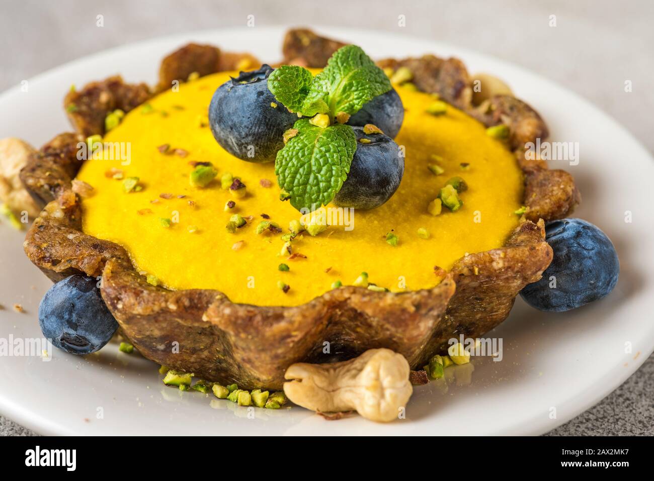 Cheesecake à la mangue brute végétalienne avec bleuets frais, menthe et pistaches. Concept de nourriture sans gluten végétalien sain. Gros plan Banque D'Images