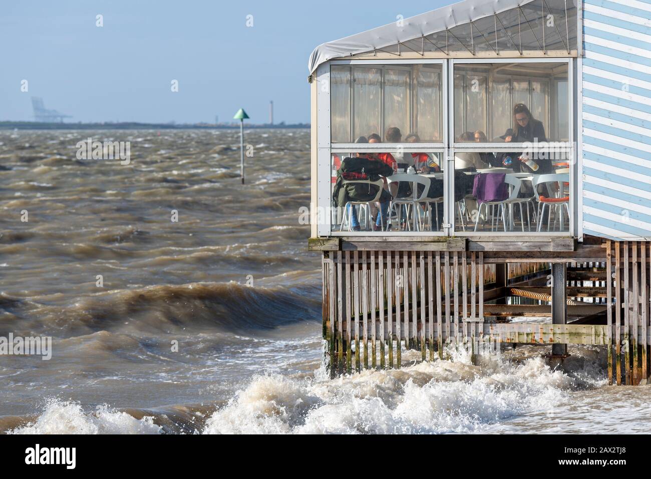 Clients et personnel du restaurant Beach Hut à marée haute et temps de tempête à Southend on Sea, Essex, Royaume-Uni. Affaires sur les fruits de mer au-dessus de l'eau Banque D'Images