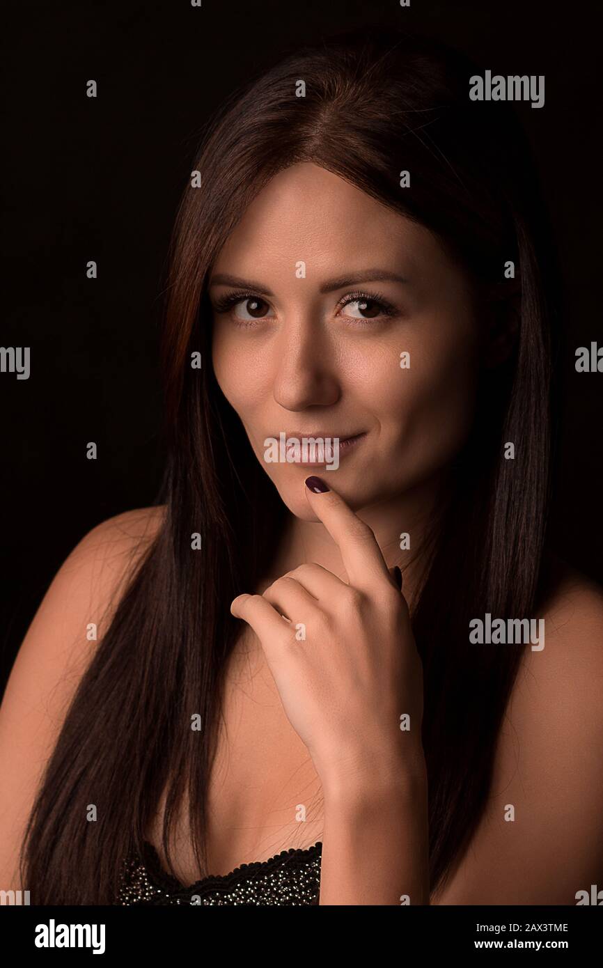 Portrait d'une belle fille, brunette à poil long qui regarde l'appareil photo et met son doigt au menton. Mystérieuse, charismatique pensive et séducti Banque D'Images