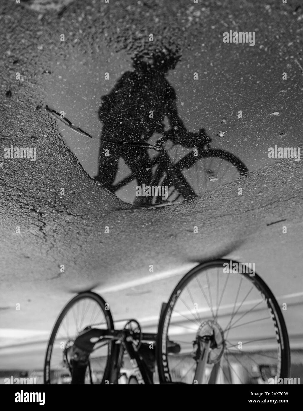 Échelle de gris du reflet d'une personne avec un vélo sur l'asphalte humide après la pluie Banque D'Images