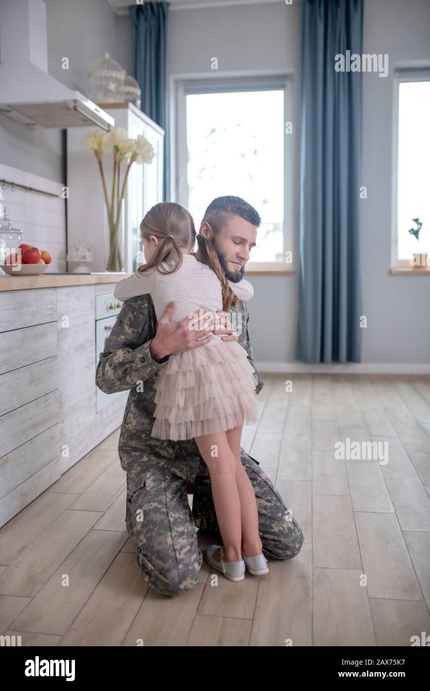 Papa en uniforme embrassant petite fille à la maison. Banque D'Images