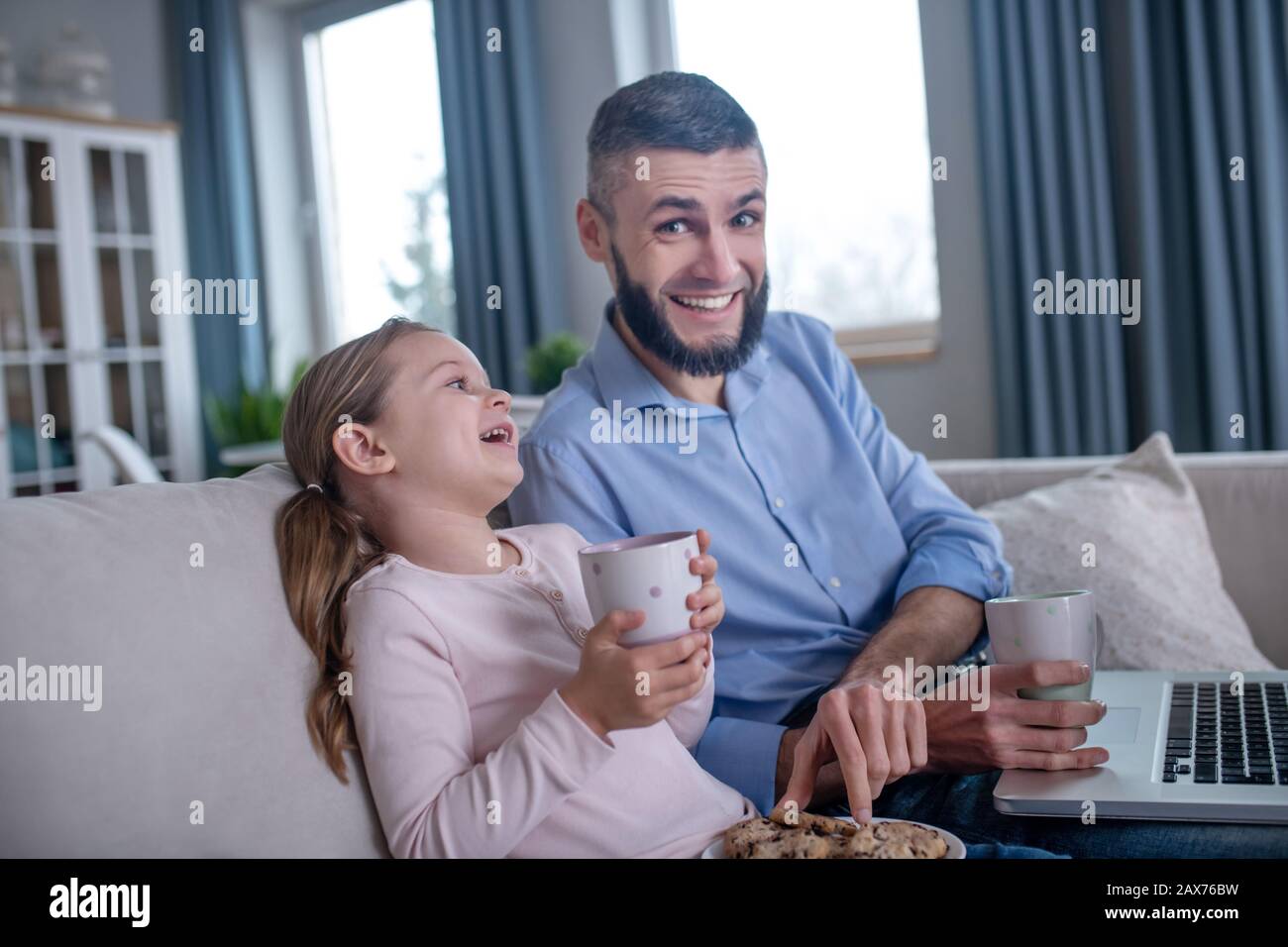 Papa et fille avec thé et cookies assis sur le canapé. Banque D'Images