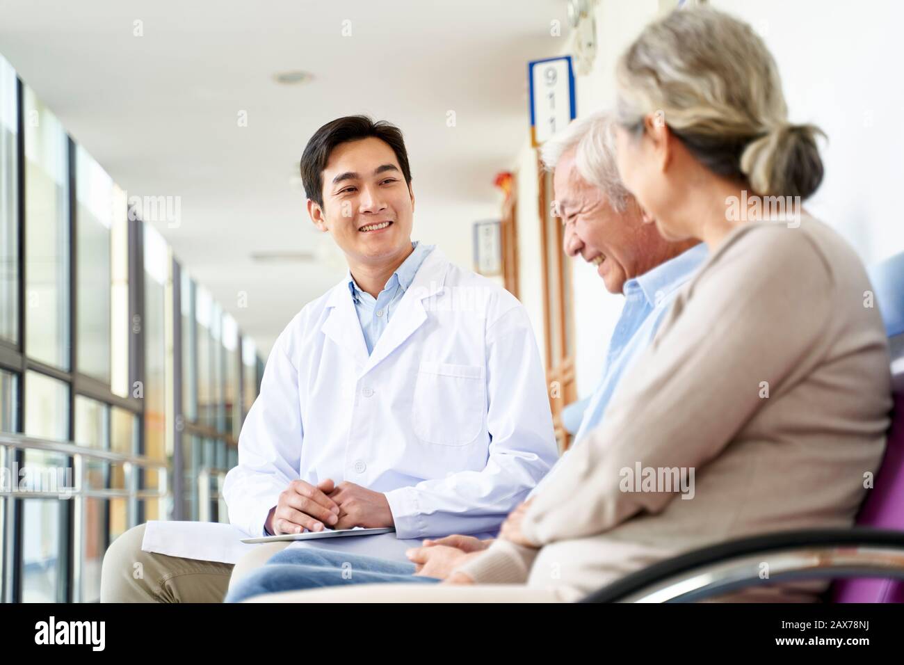 sympathique jeune médecin asiatique parlant à un vieux couple dans le couloir de l'hôpital Banque D'Images