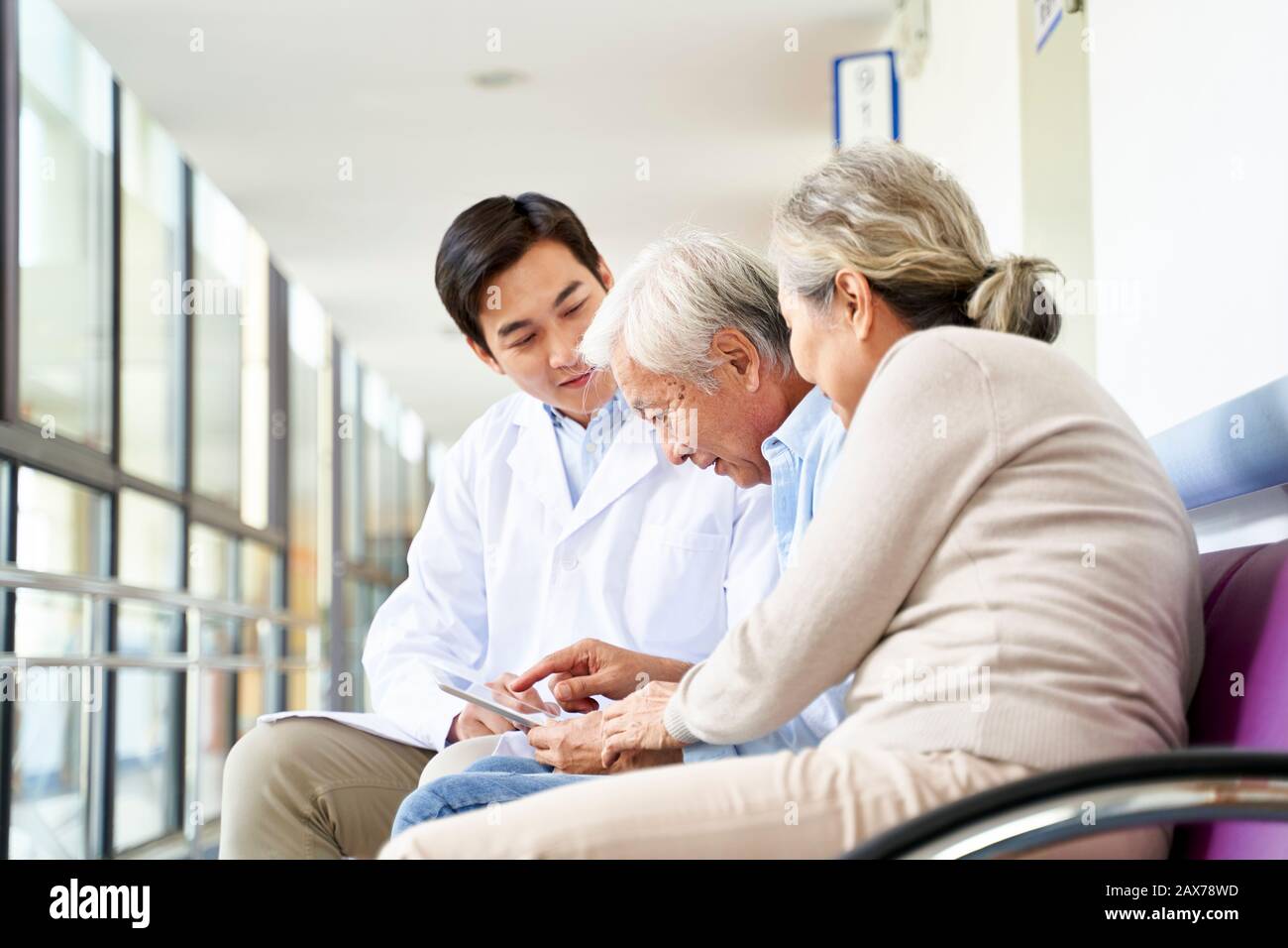 un jeune médecin asiatique discute du résultat du test et du diagnostic avec des patients de couple senior utilisant une tablette numérique dans le couloir de l'hôpital Banque D'Images