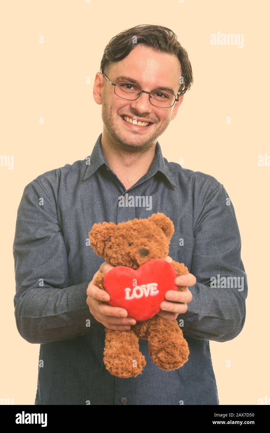 Studio shot of young happy man smiling formelle tout en maintenant l'ours en peluche avec coeur et amour sign Banque D'Images