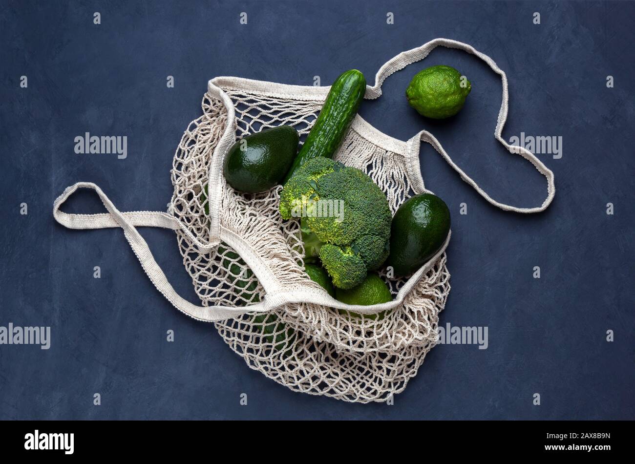 Sac réutilisable avec légumes verts sur fond bleu foncé. Sac en maille à cordes, concept sans plastique, vue du dessus Banque D'Images