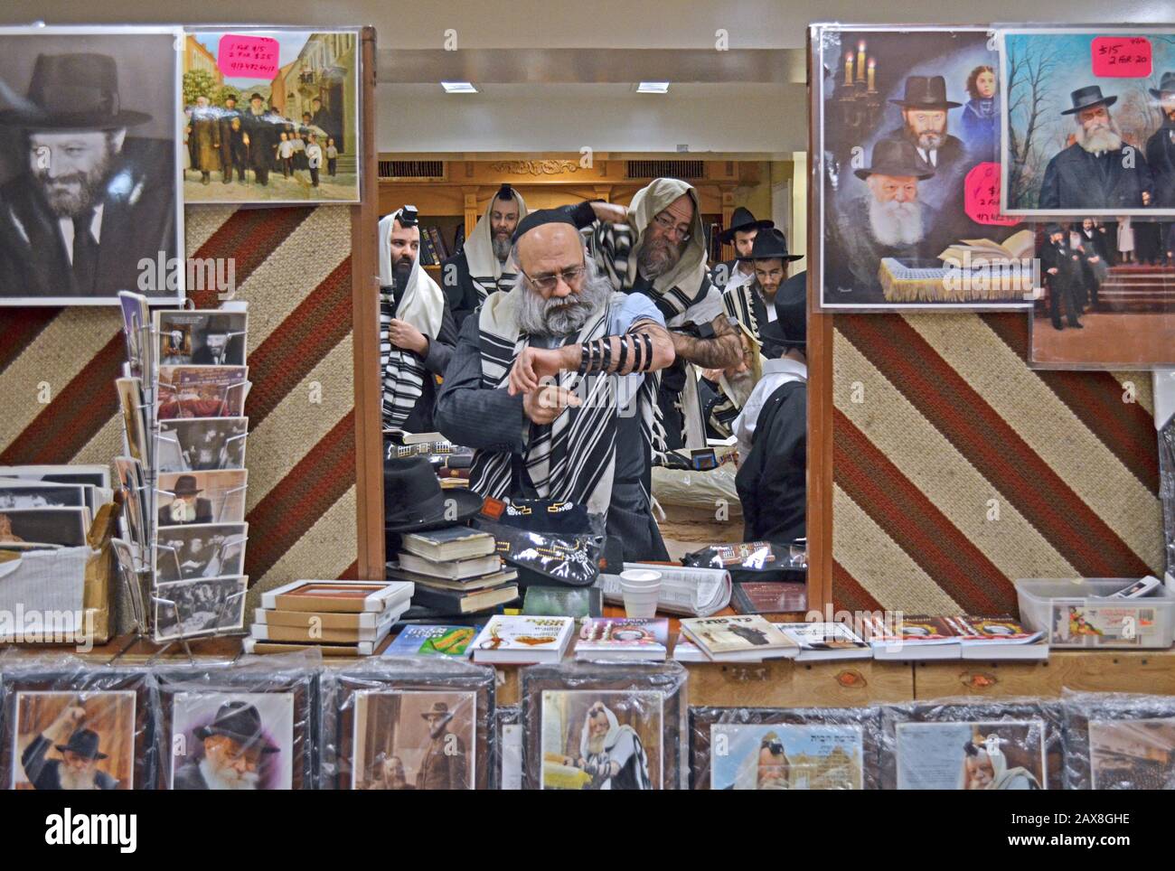Un juif orthodoxe met sur son tefillin derrière un mur de photos du Lubavitcher Rebbe qui sont en vente, À Brooklyn, New York City. Banque D'Images