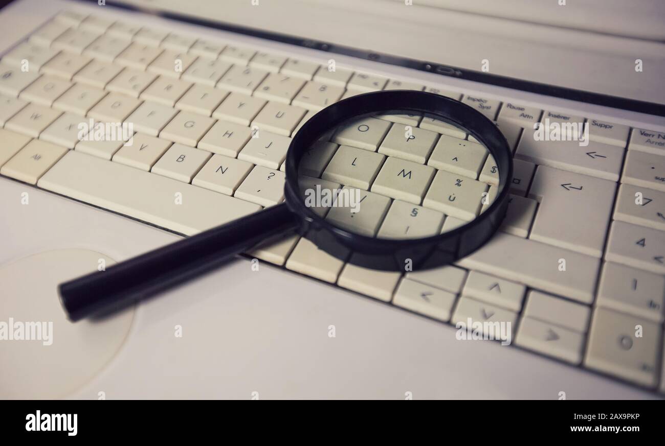 Gros plan d'une loupe sur un ancien clavier d'ordinateur portable. Moteur de recherche d'ordinateur. Parcourir le réseau pour répondre à chaque question. Trouver des informations utiles Banque D'Images