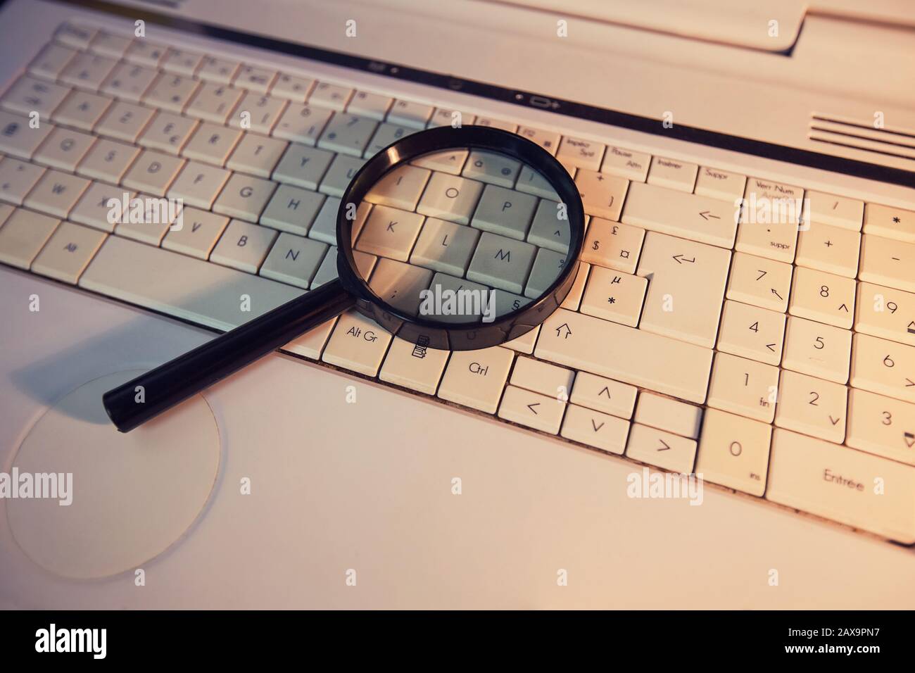 Gros plan d'une loupe sur un ancien clavier d'ordinateur portable. Moteur de recherche d'ordinateur. Parcourir le réseau pour répondre à chaque question. Trouver des informations utiles Banque D'Images