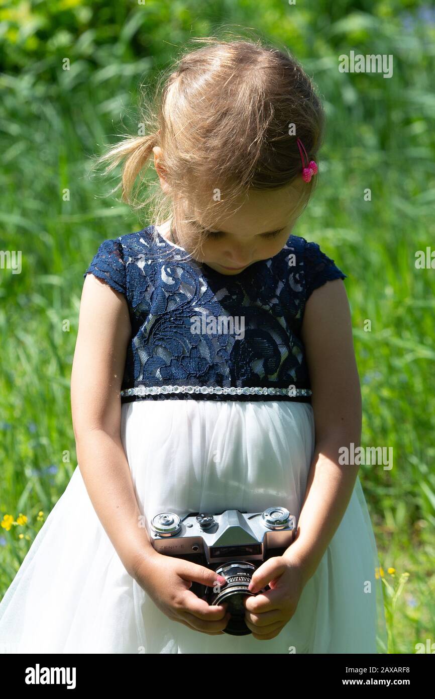Petite fille mignonne dans une robe légère tenant un appareil photo rétro  vintage dans une triste humeur. Petite fille avec un appareil photo rétro  dans le parc en été. C Photo Stock -