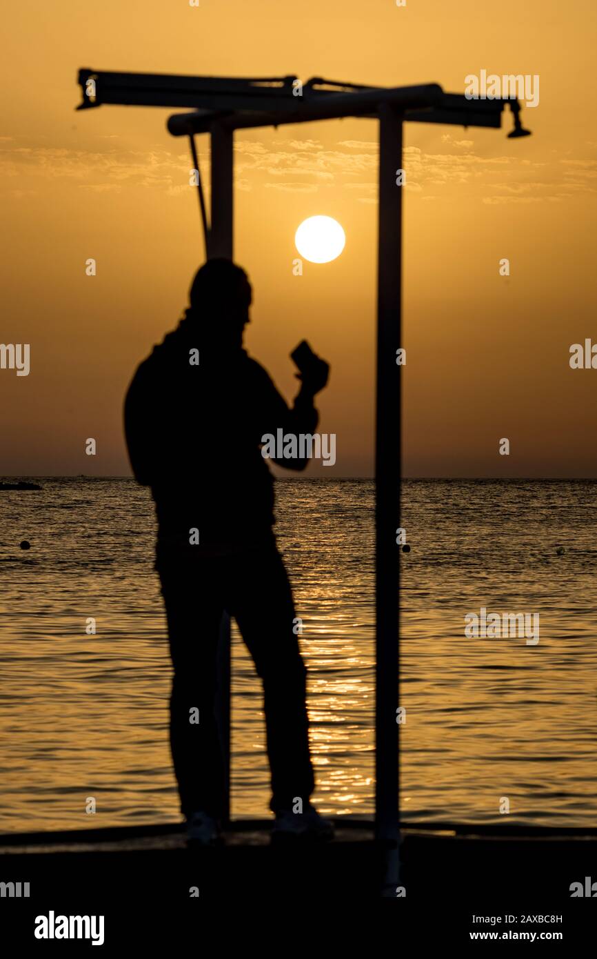 Concentrez-vous sur le soleil. Silhouette Floue de l'homme inconnu avec  téléphone prenant des photos au coucher du soleil devant l'eau de la mer  Ionienne dorée près de la plage. Crépuscule vu de