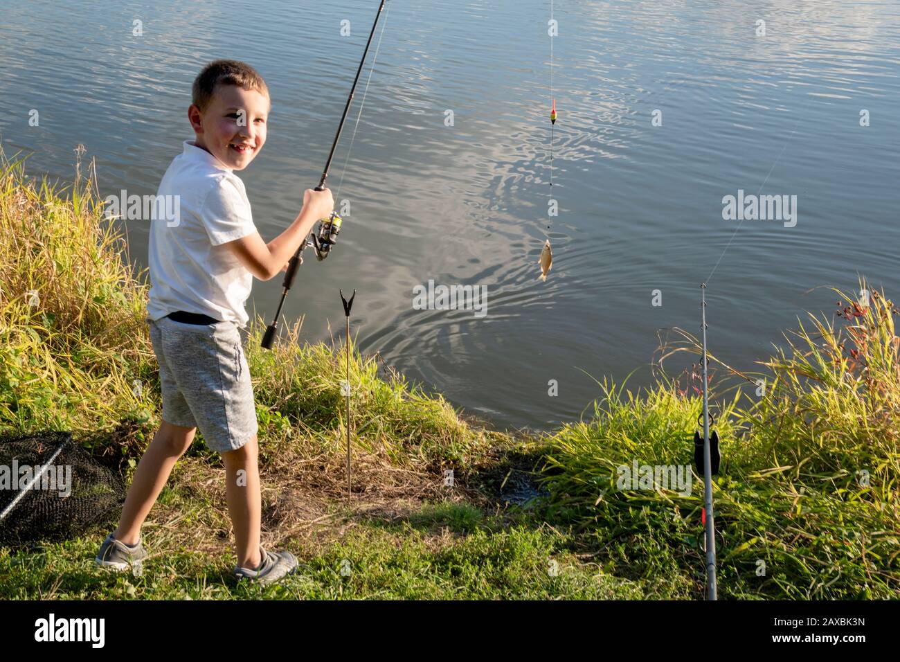 Un heureux garçon a pris un poisson. Pêche de garçon sur un lac. Tige de pêche pour enfant. Petit pêcheur. Banque D'Images