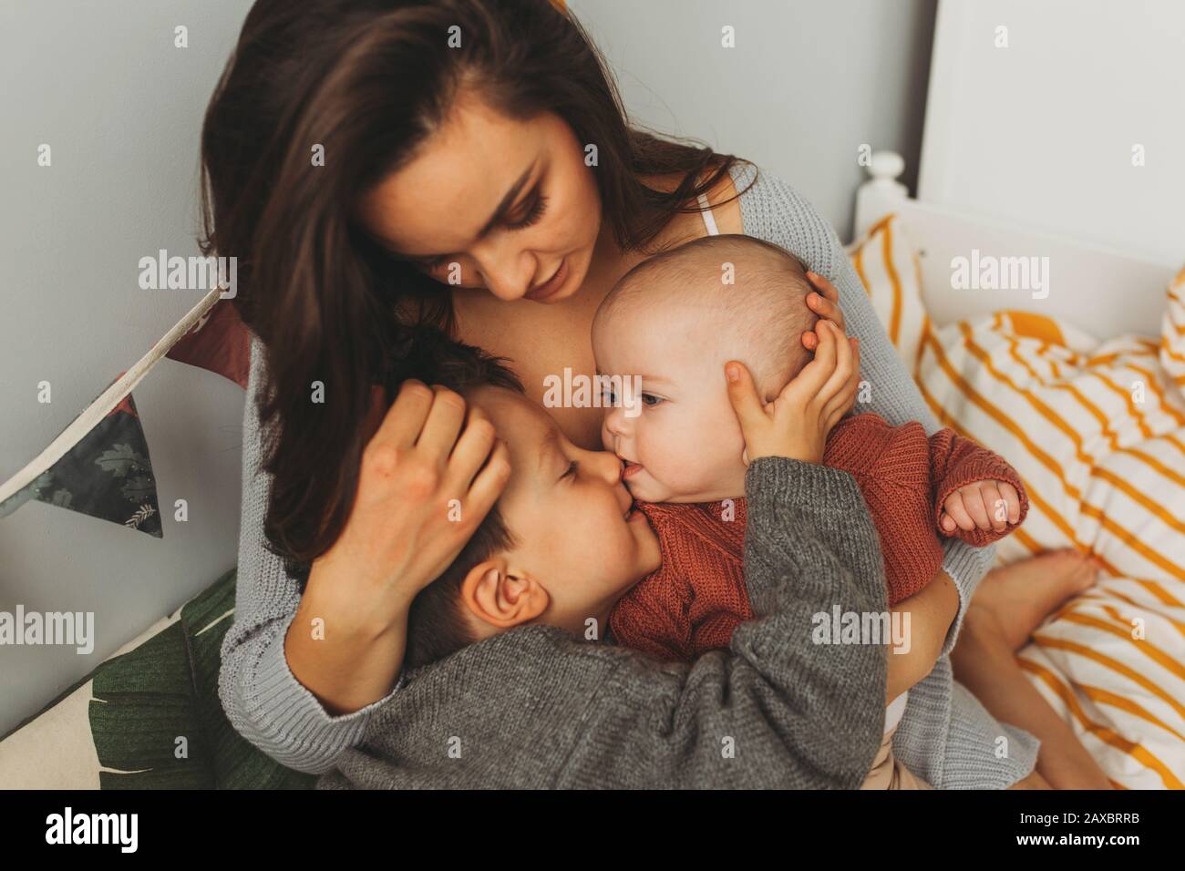 Jeune belle mère avec ses enfants sur le lit, étroitement embrasse son fils et fille, embrasse son front, les enfants rient Banque D'Images