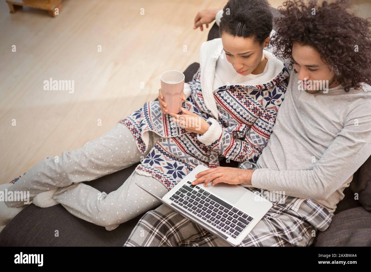 Couple affectueux dans un pyjama relaxant, utilisant un ordinateur portable sur un canapé Banque D'Images