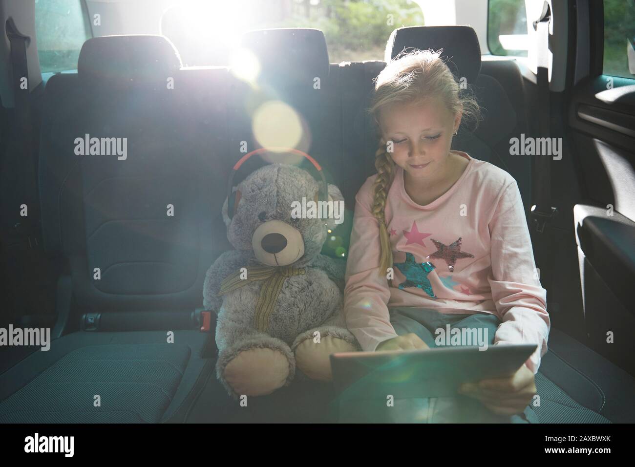 Fille avec ours en peluche utilisant une tablette numérique dans le siège arrière de la voiture Banque D'Images