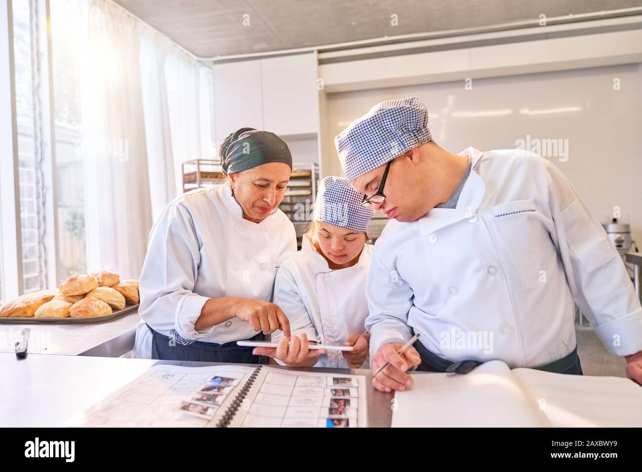Chef et étudiants avec syndrome De Down utilisant tablette numérique dans la cuisine Banque D'Images
